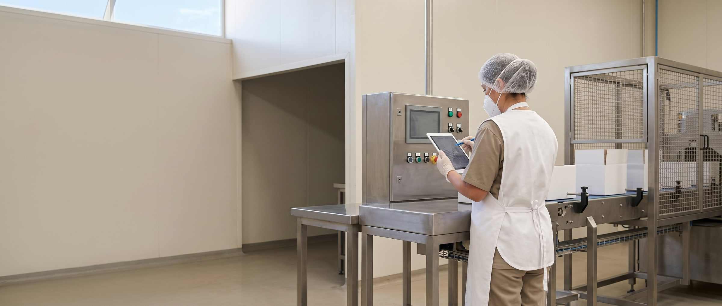 A quality technician, seen from behind, at a stainless steel table in a food processing room.