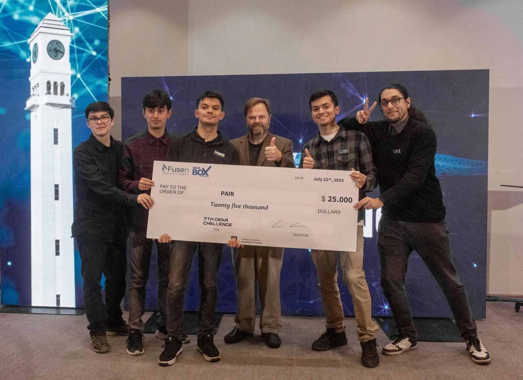 The PAIR team on stage holding the symbolic twenty-five-thousand-dollar cheque of the 7th Gear Challenge, with the Fusen and Gearbox marks.